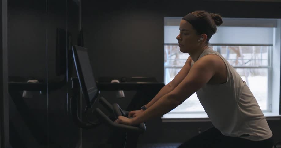 A woman at home touches a screen on her stationary bike as she starts to exercise