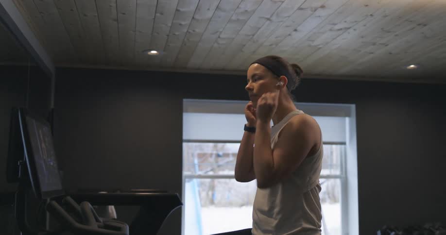 A woman riding a stationary bike at home puts ear buds in