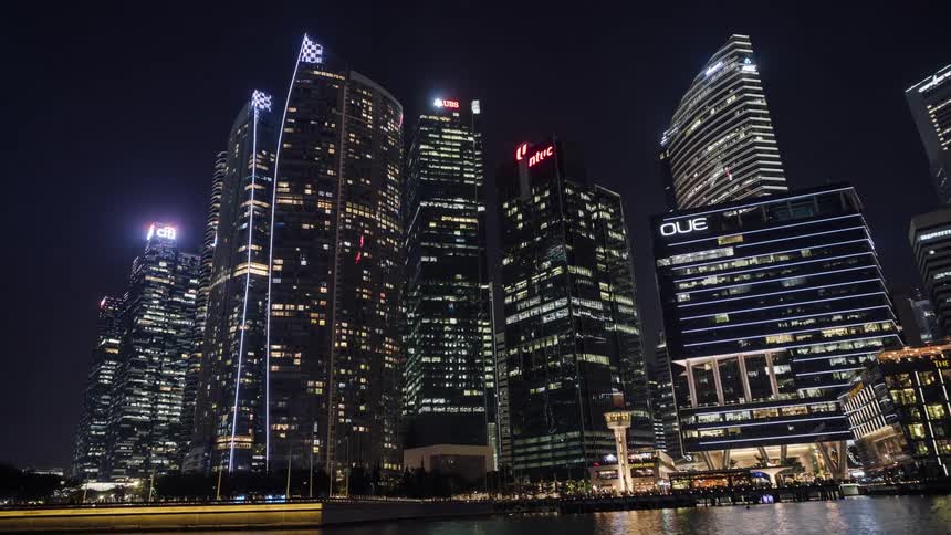 Illuminated city skyscrapers next to sea seen from traveling boat at night