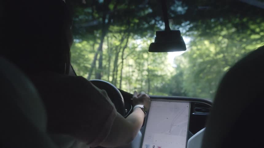 A woman points at a map on a tablet in her car as she drives