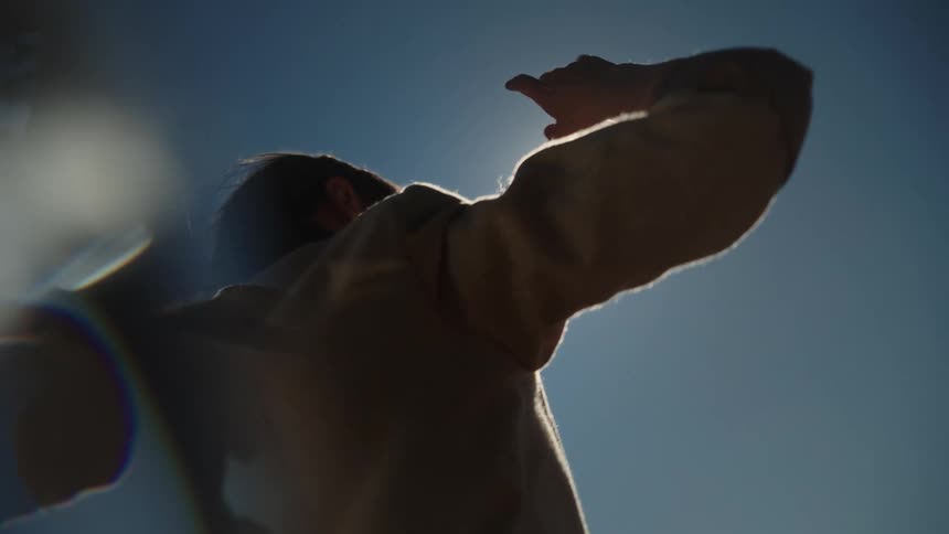 Young woman dancing under the flares of a bright sunlight on a blue sky