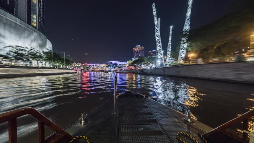 Time lapse of a boat moving through the colorful illuminated city on the singapore river at night