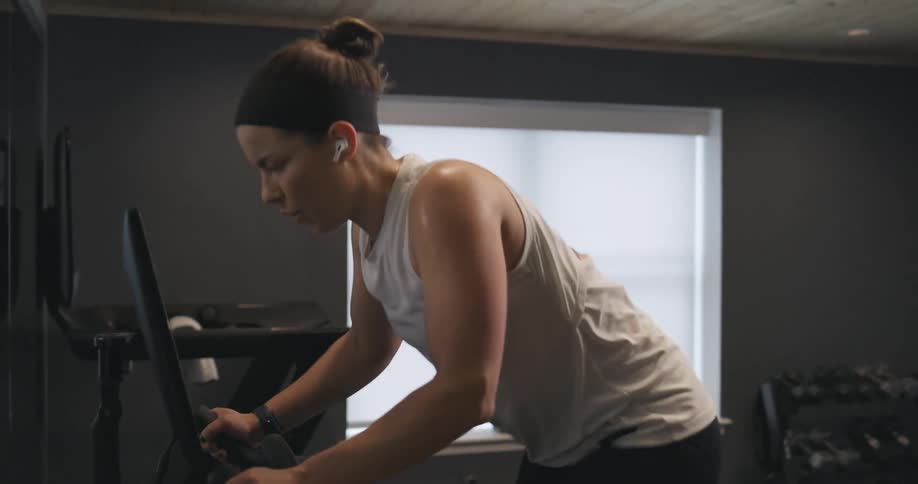 Woman covered in sweat wearing sports clothes working out over a static bicycle at home