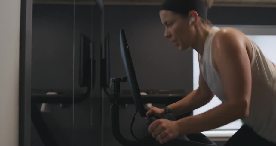 Woman covered in sweat wearing sports clothes working out over a static bicycle at home