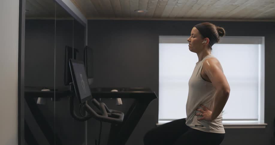 Woman covered in sweat wearing sports clothes working out over a static bicycle at home