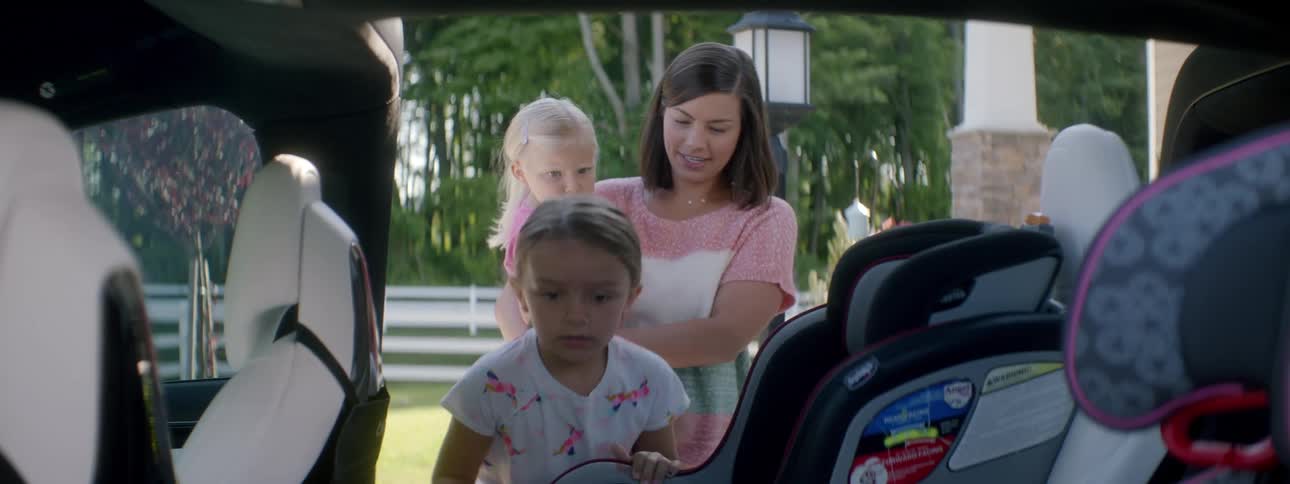 A woman opens the door to her minivan while carrying her daughter