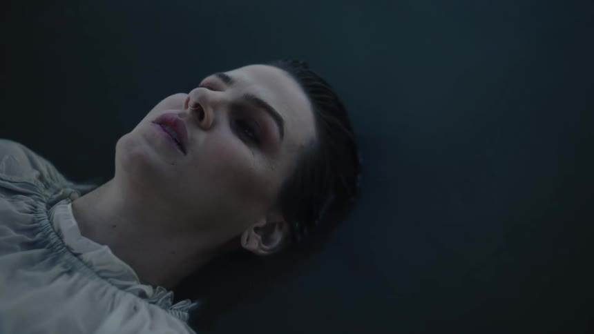 Close up of the face of a woman wearing a white gown floating over dark water
