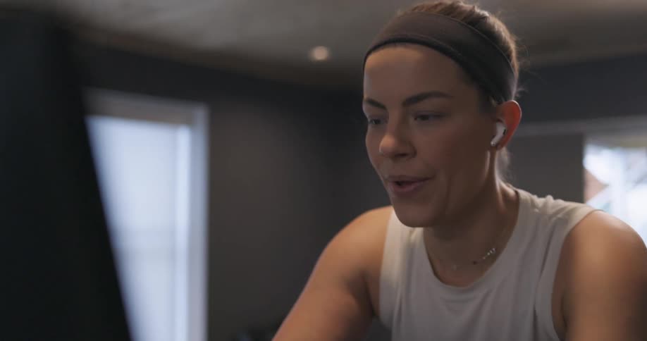 Woman covered in sweat wearing sports clothes working out over a static bicycle at home