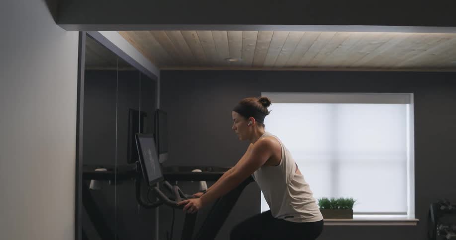 Woman covered in sweat wearing sports clothes working out over a static bicycle at home