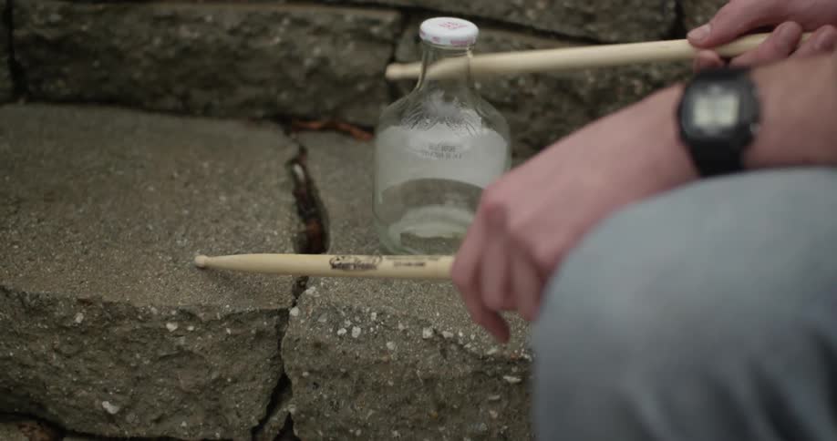 Close-up of a street performer using his drumsticks to tap a bottle and concrete