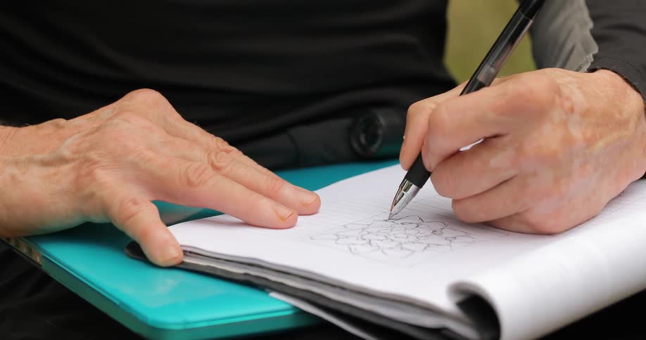 A man is drawing in a notebook with a pen