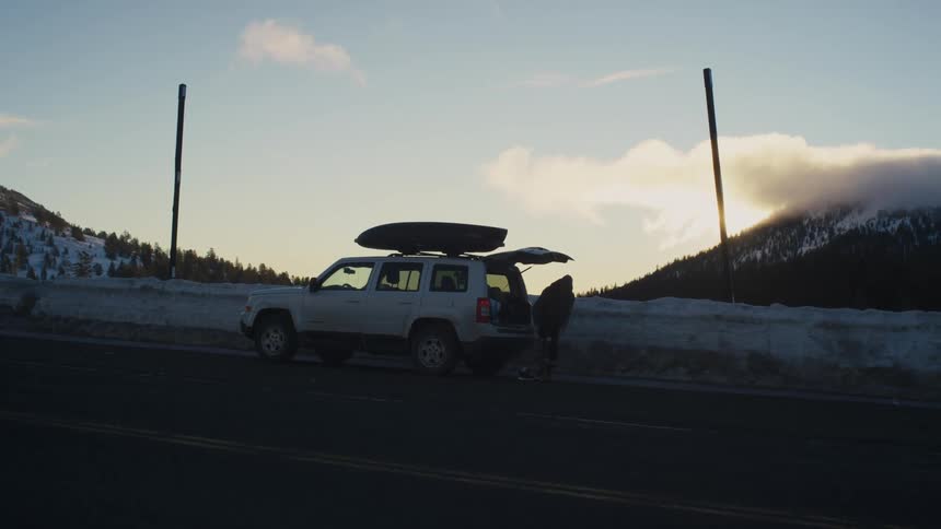 A person looks out over a snow covered landscape as their vehicle is parked next to the side of a road