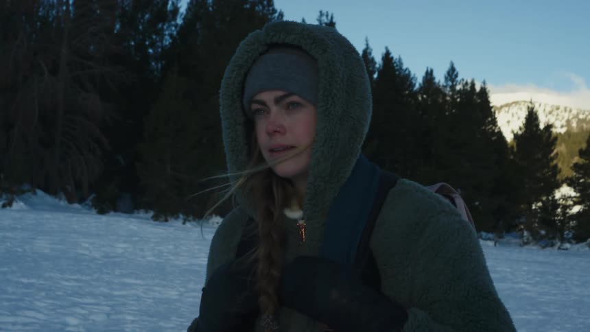 Woman with green wooly hat jacket and backpack walks in snowy field next to forest