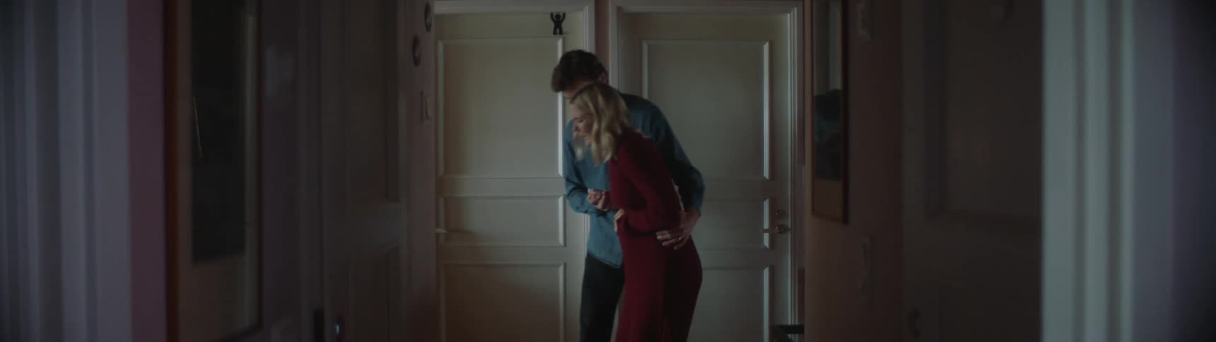 Man with blue shirt helps blonde pregnant woman in red dress walk in house