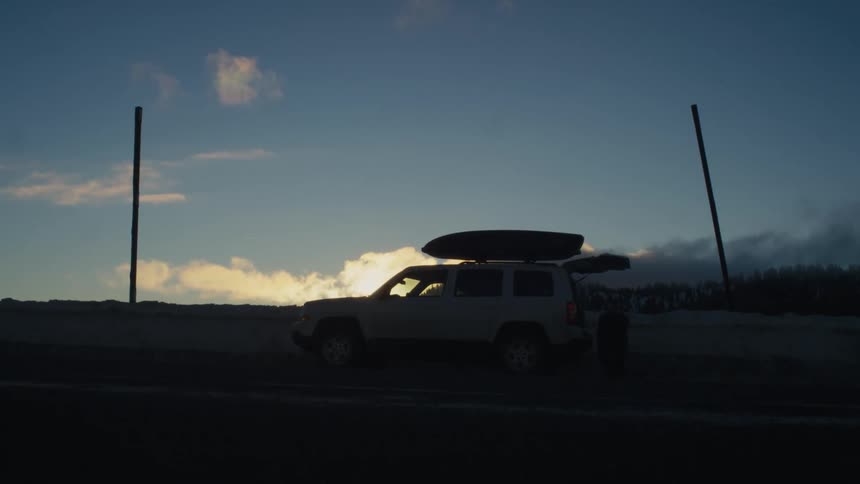 A man stands behind his vehicle on the beach
