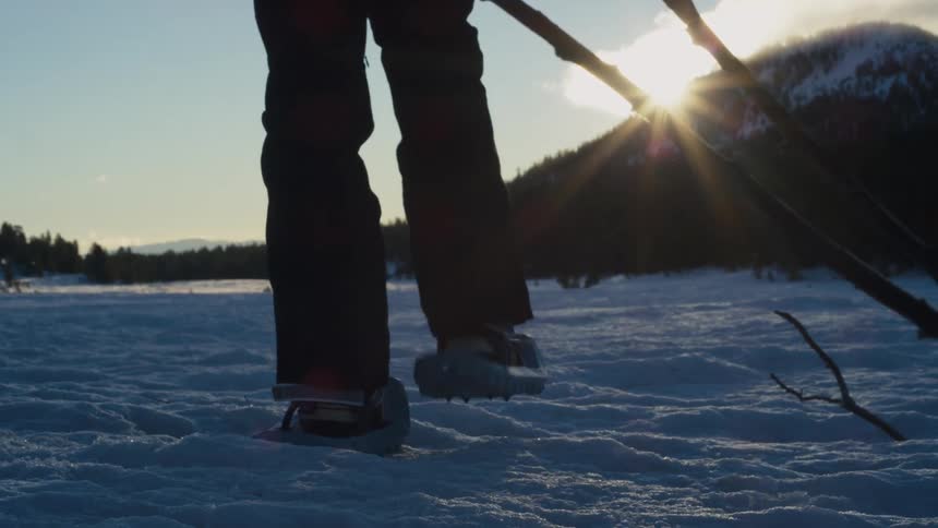 A person walks through a snowy field in the wilderness using snow shoes during the day