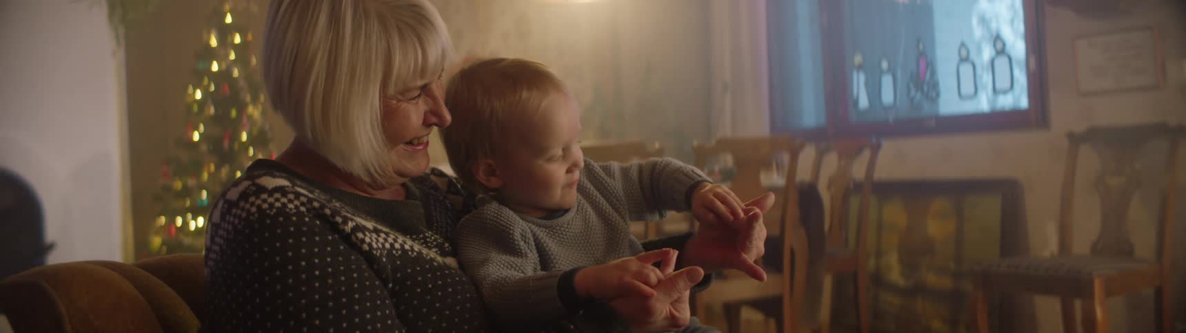 Grandma sitting with her little grandson on her lap smiling as he happily plays with her fingers
