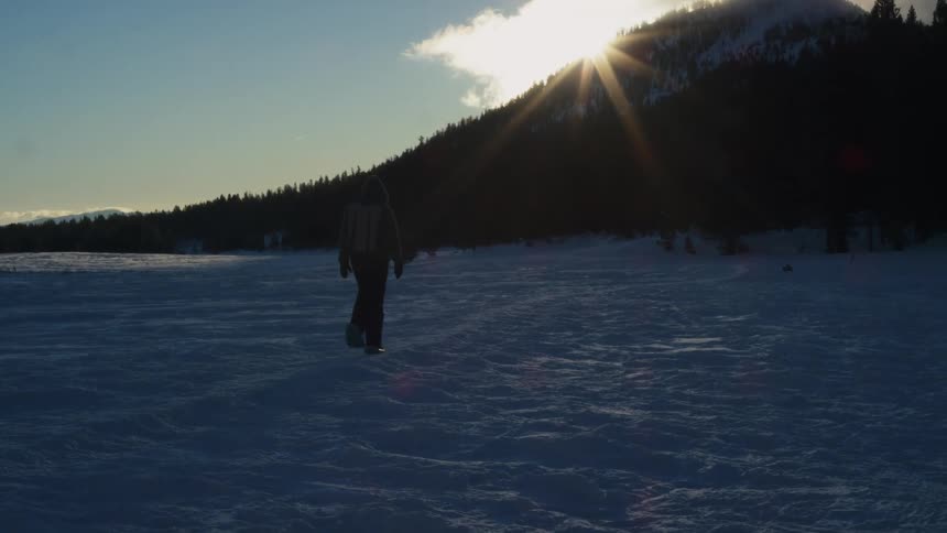 Silhouette of a man walking on the snow towards a forest in the mountains at morning
