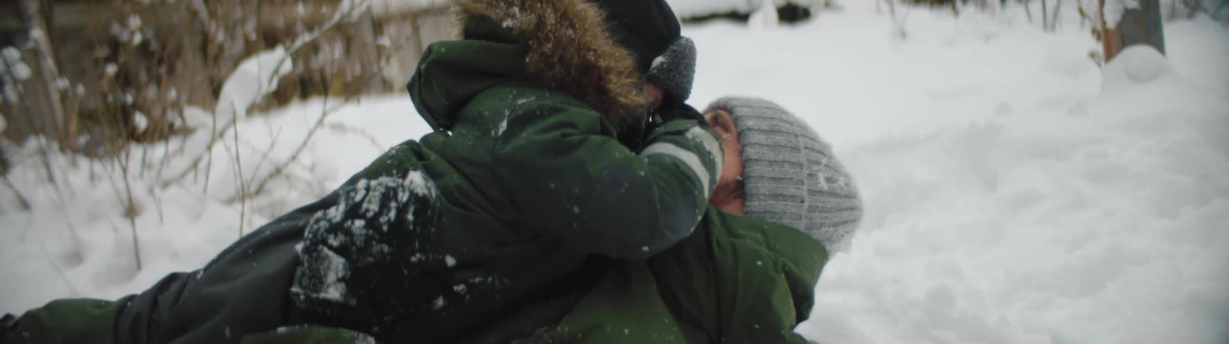 Dad lying on his back in the snow with his little boy on top playing