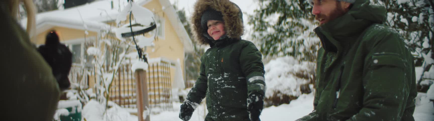Father mother and son wearing winter clothes playing in the snow making snowballs and throwing at each other