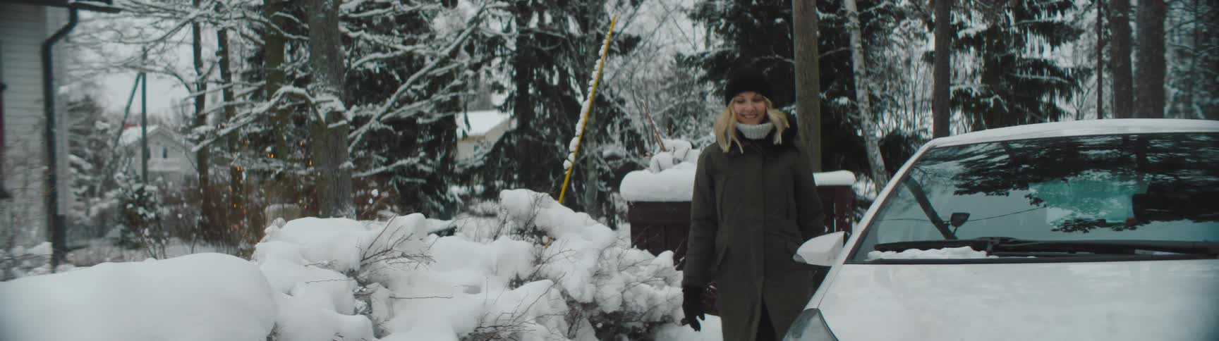 A woman climbing out of a parked car and smiling on a cold winter day