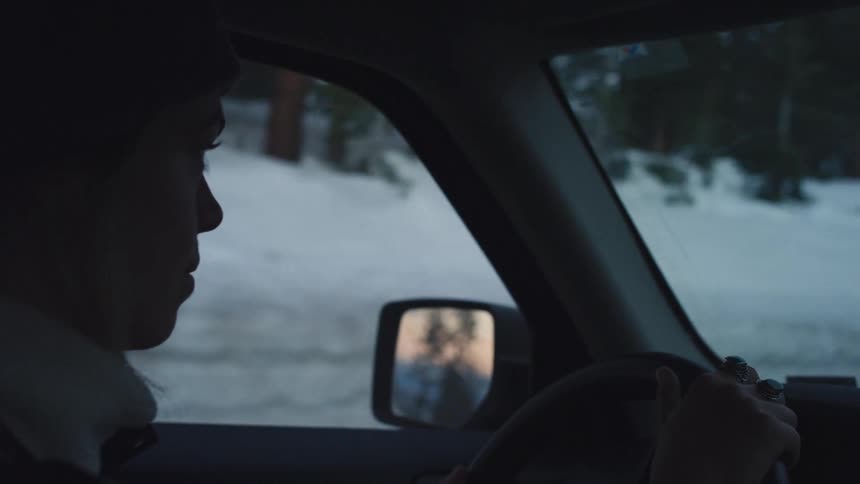 A woman driving a car on a snowy winter evening