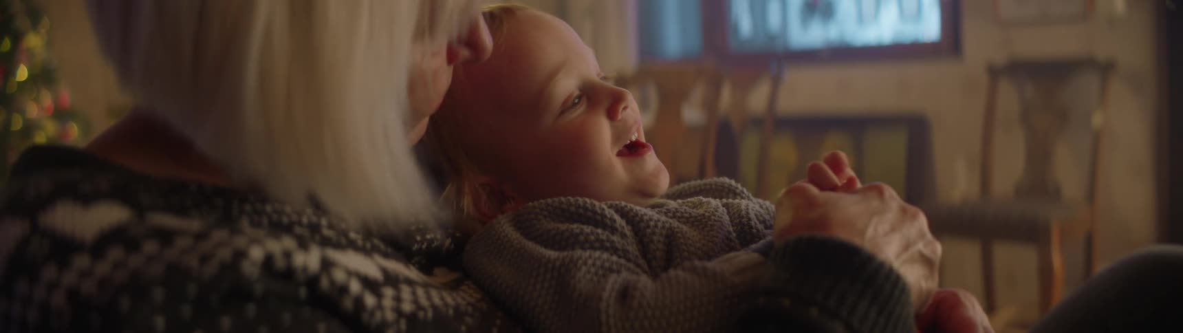 A grandmother with gray hair holding her grandchild indoors