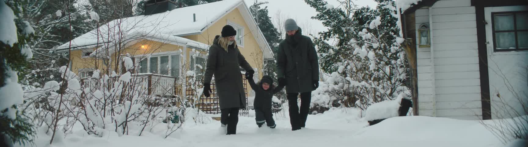 Mom and dad holding their sons hands as they walk and play in the snow covered yard
