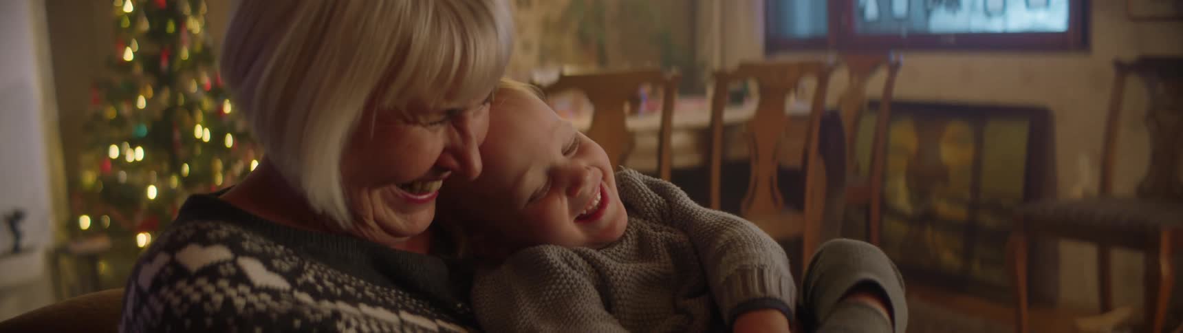 A woman tickles a child while holding the child in her arms as she sits indoors