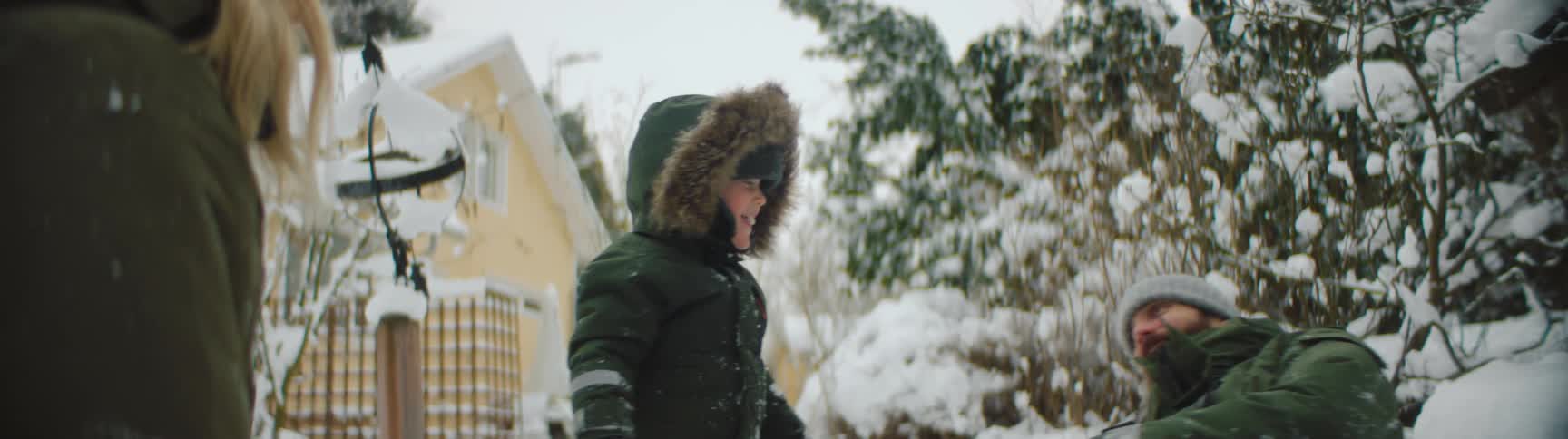 Family wearing thick winter clothes playing with snow near a house in the countryside