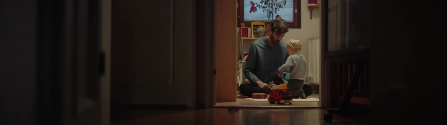 Father sits on floor in room playing with toys with his son
