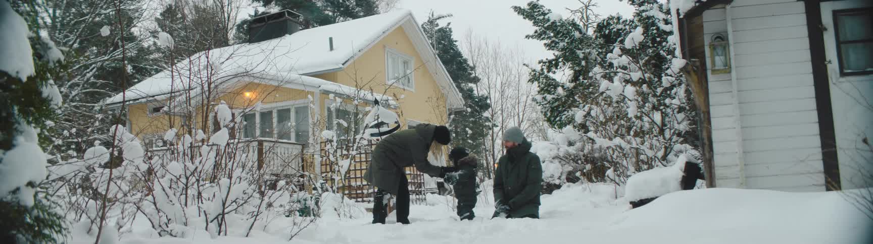 A man and woman throw snow and play with their child outside their home