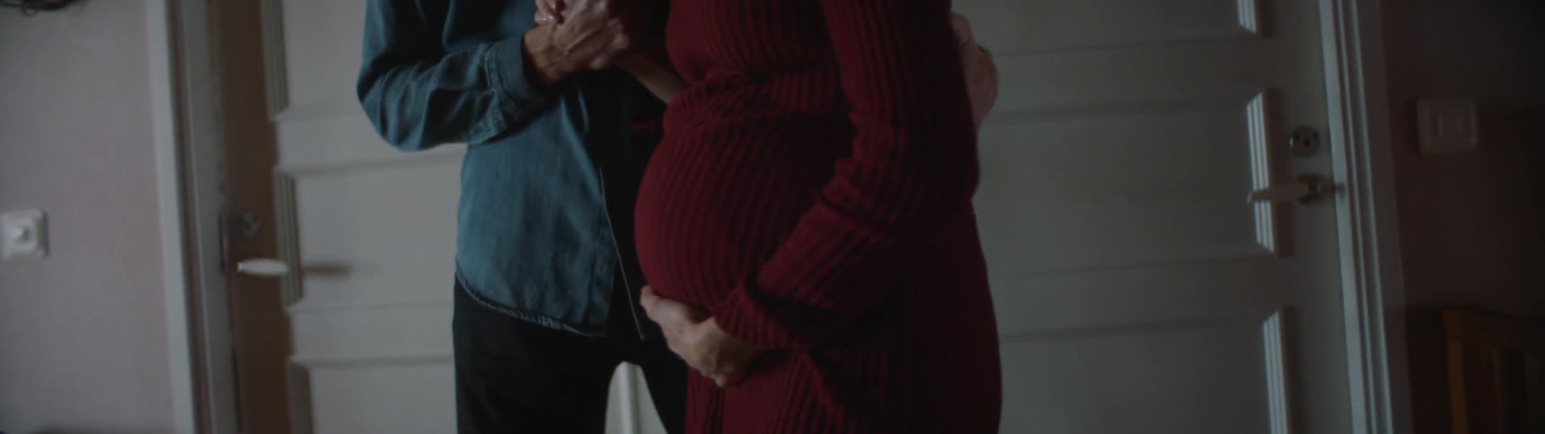 Man helps pregnant woman walk across room as she rubs her belly