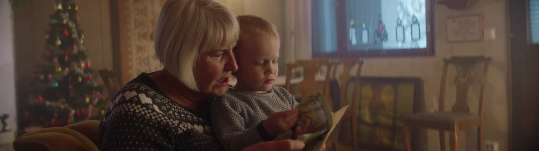 Grandmother and grandson sit in living room at christmas reading a book together