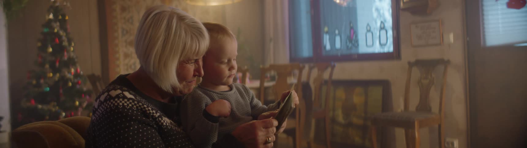 Grandmother sits with boy in her lap reading to him with a christmas tree in the background