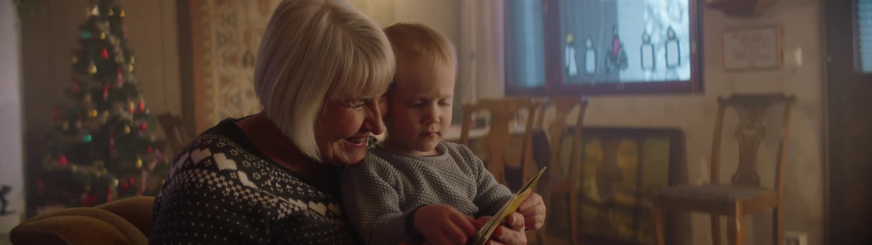 Grandmother reading a story to her grandson on the living room at home near a christmas tree