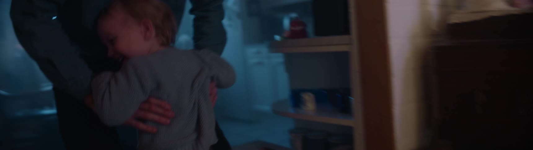 Male toddler smiles and runs to his father who then picks him up as a christmas tree stands on the other side of the room
