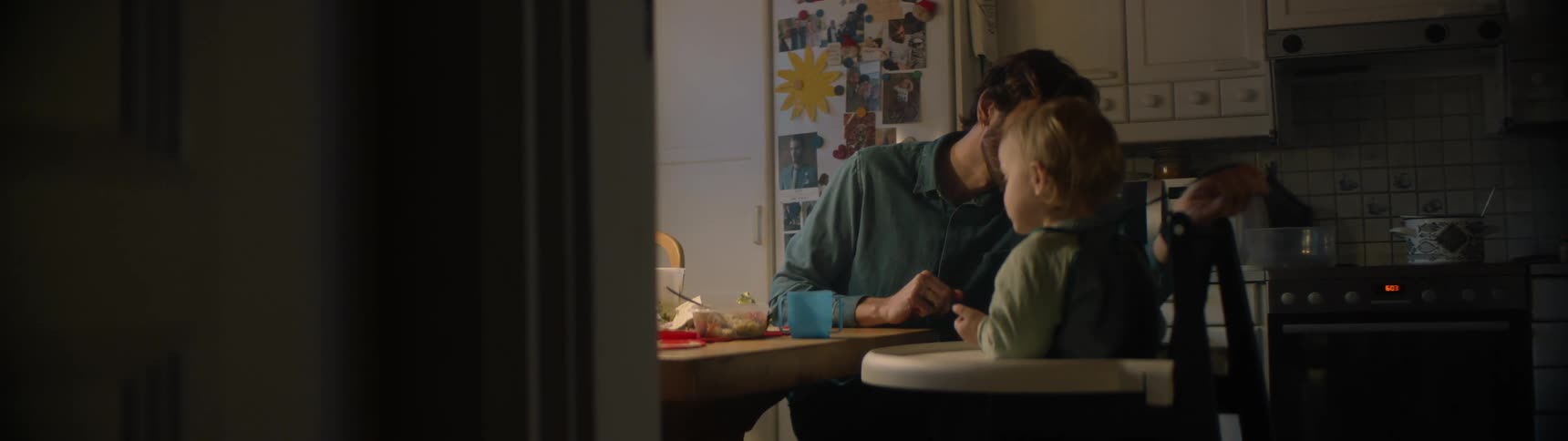 Father unties bib of son sitting in highchair at table in kitchen