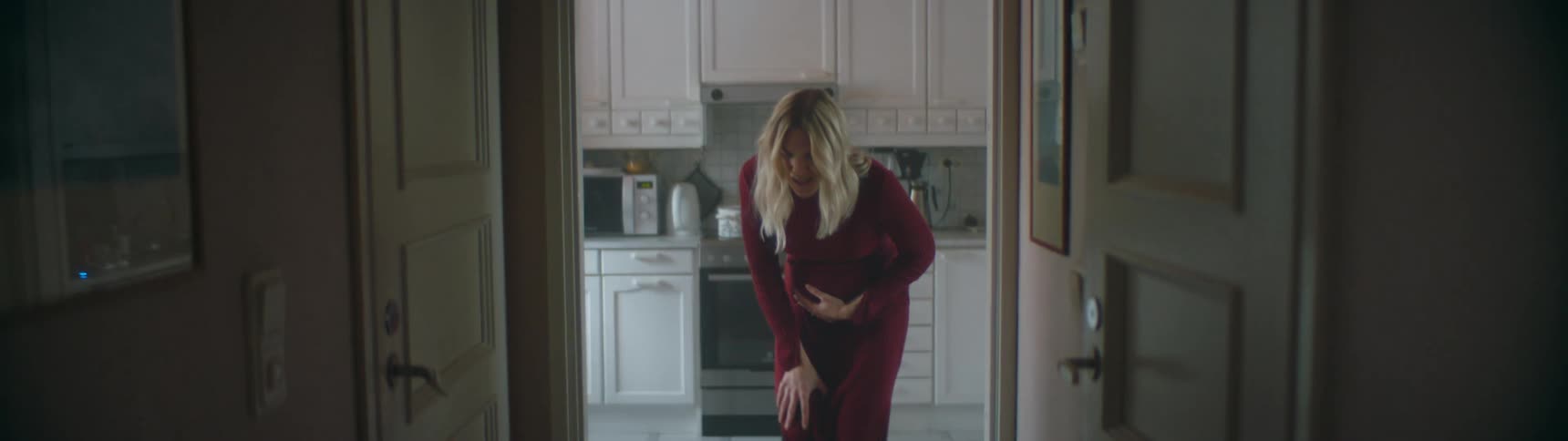 A pregnant woman at home grabs her belly and calls out as she bends over and her husband runs over to help her