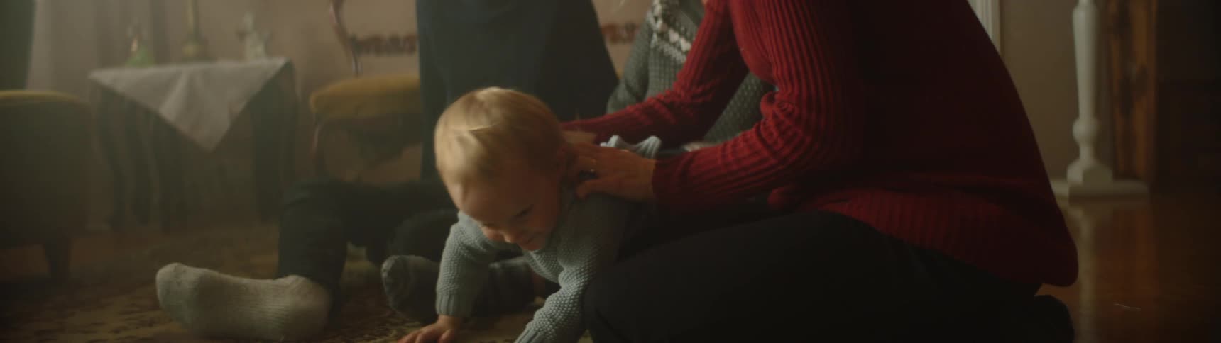 Toddler boy crawls around pregnant mother and grandmother next to father wit beard in living room at home
