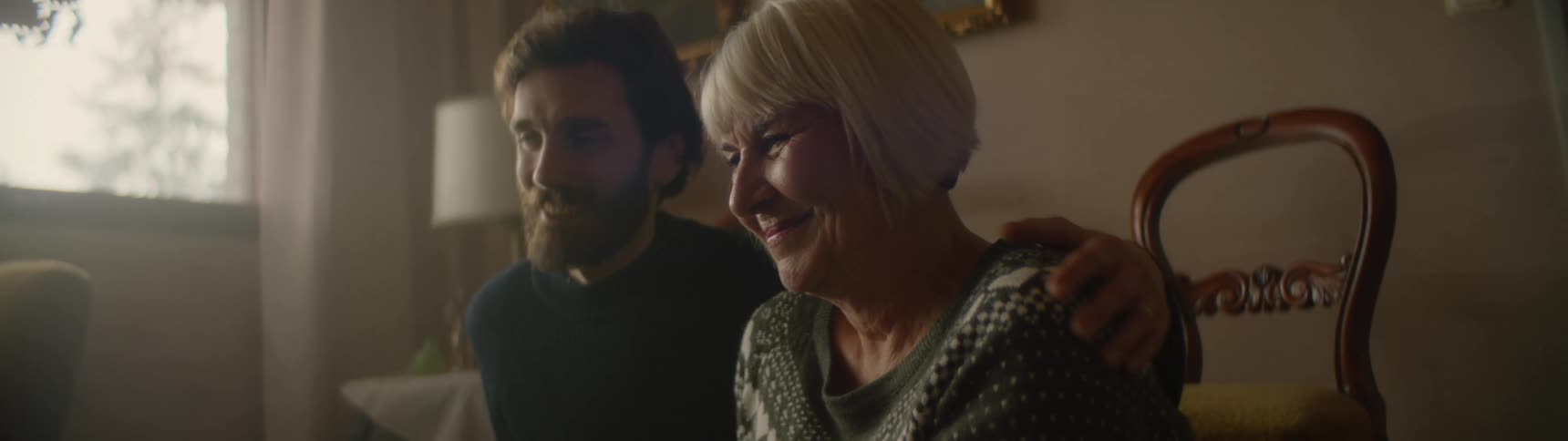 Son hugs mother as he and she sit smile and talk