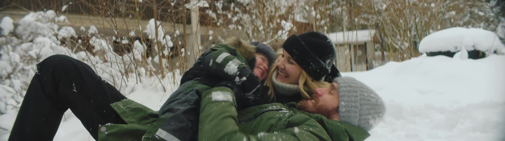 Family wearing thick winter clothes playing with snow on the ground near a house at winter