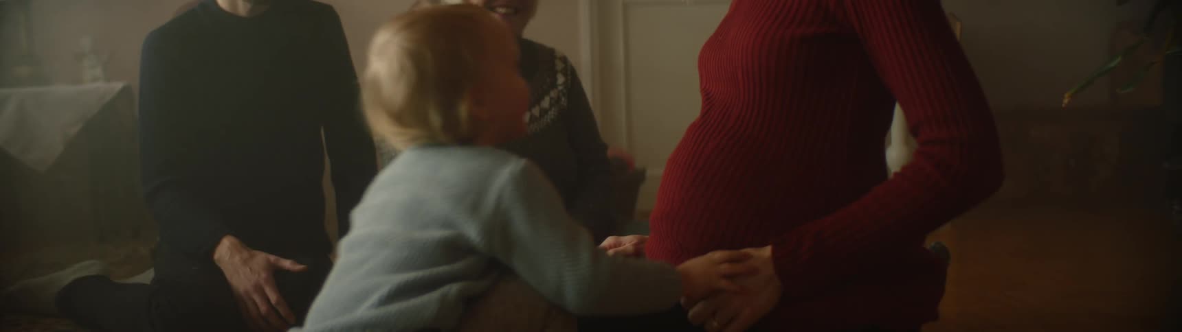 Young boy kisses moms pregnant abdomen before walking toward his father and grandmother