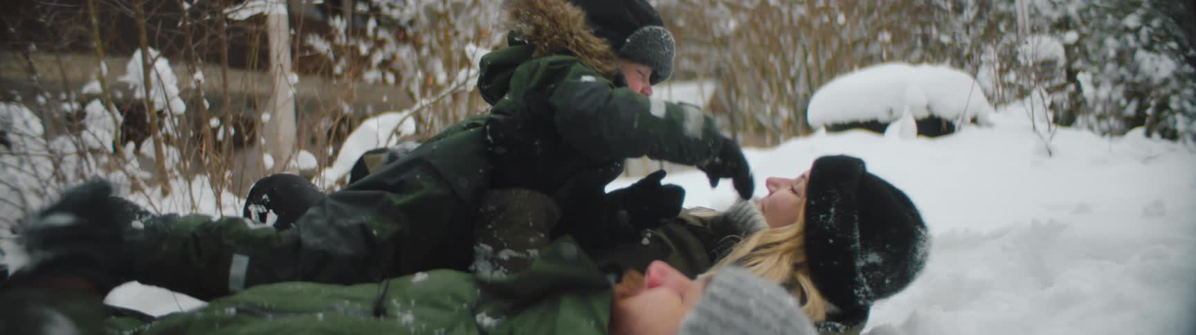 Family wearing thick winter clothes playing with snow on the ground near a house at winter