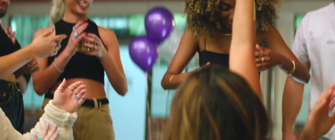 A woman dances at a party and her friends cheer her on and clap