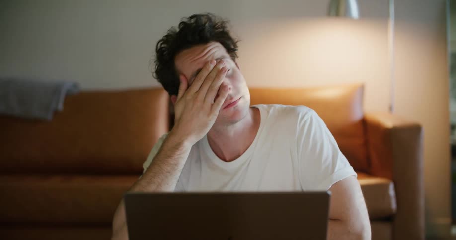 A man appears to be frustrated as he looks at his laptop before finally closing it