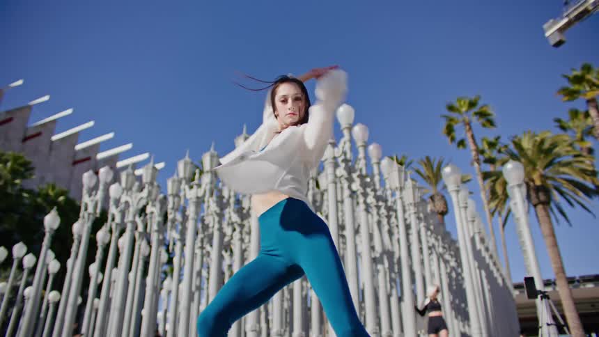 A pale white woman waves her arms as she performs a series of dance moves outdoors
