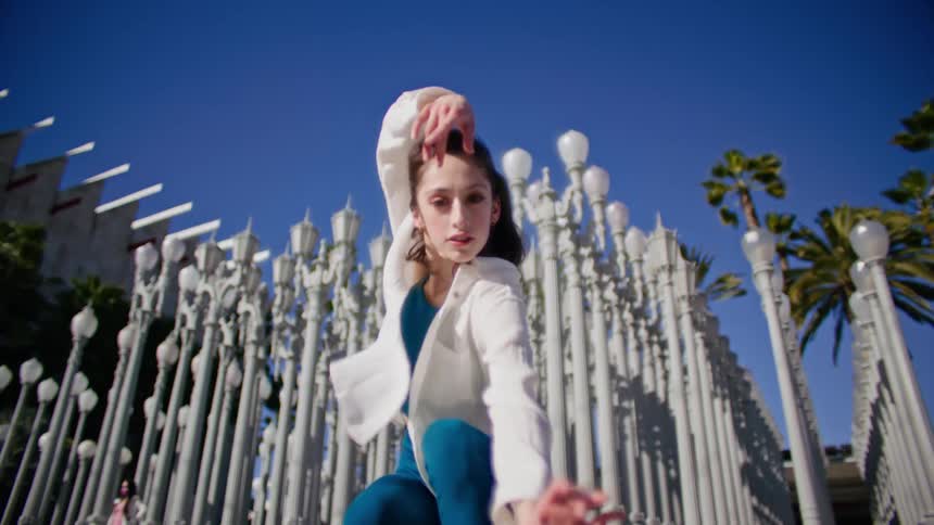 Young woman energetically dancing in front of streetlamp on a park in the city