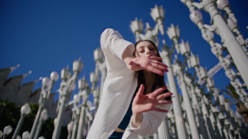 Young woman energetically dancing in front of streetlamps on a park in the city