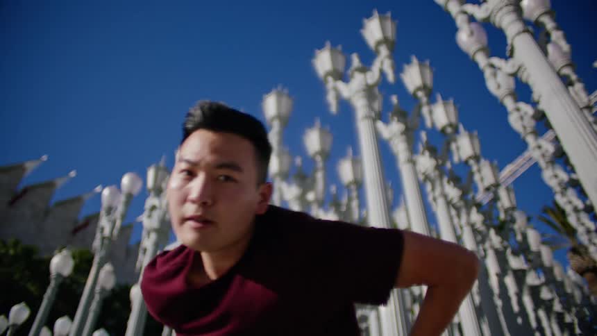 Young asian man energetically dancing in front of a street lamps on a park under a blue sky